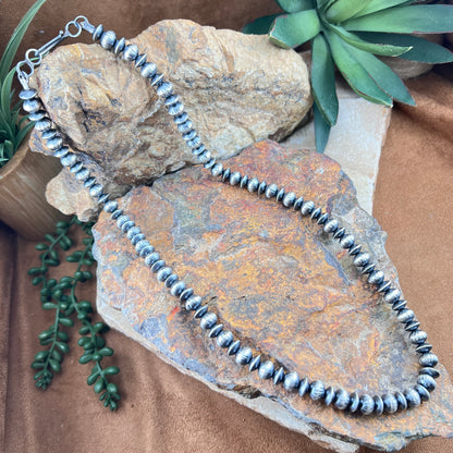 Silver beaded necklace on a textured stone surface with greenery