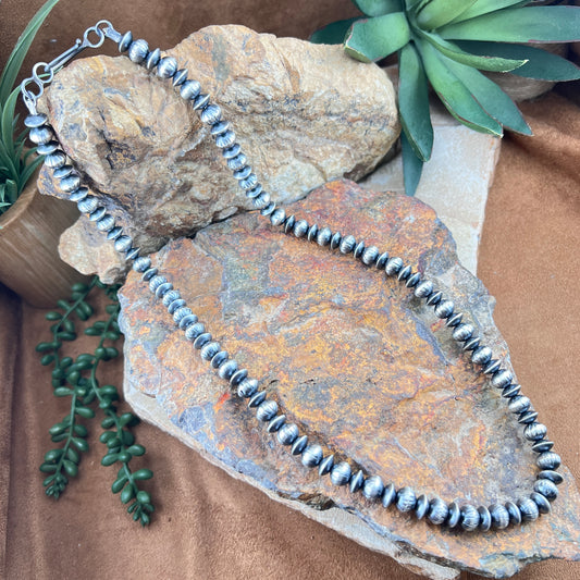 Silver beaded necklace on a textured stone surface with greenery
