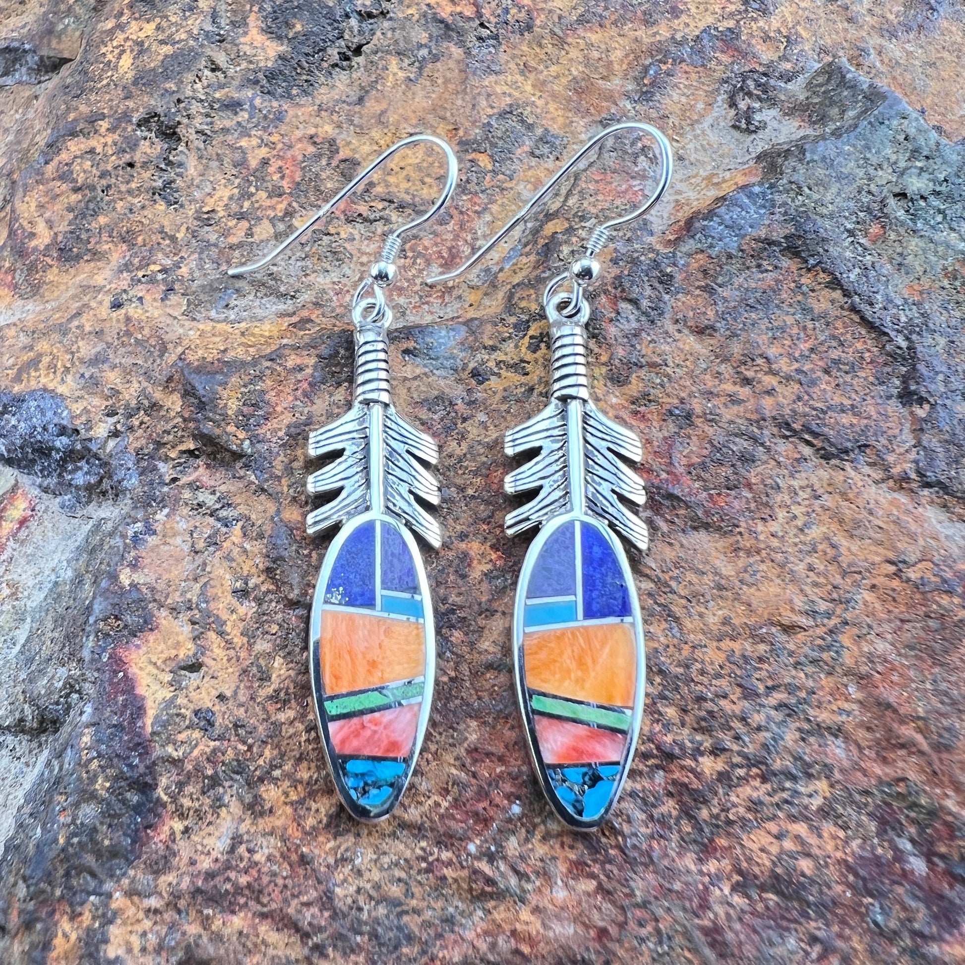 Silver feather-shaped earrings with colorful inlay on a stone background