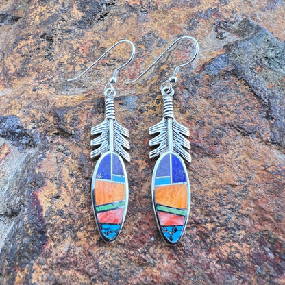 Silver feather-shaped earrings with colorful inlay on a stone background