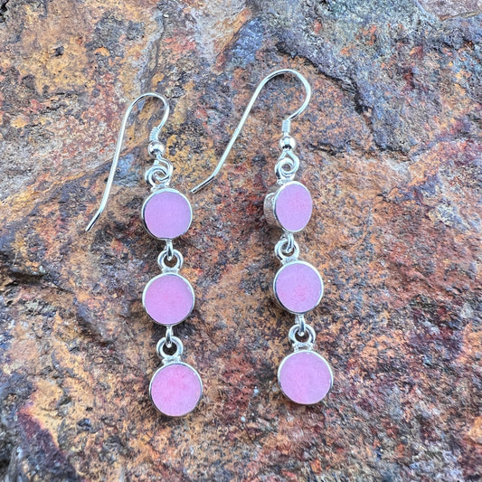 Silver earrings with pink circular stones on a stone surface