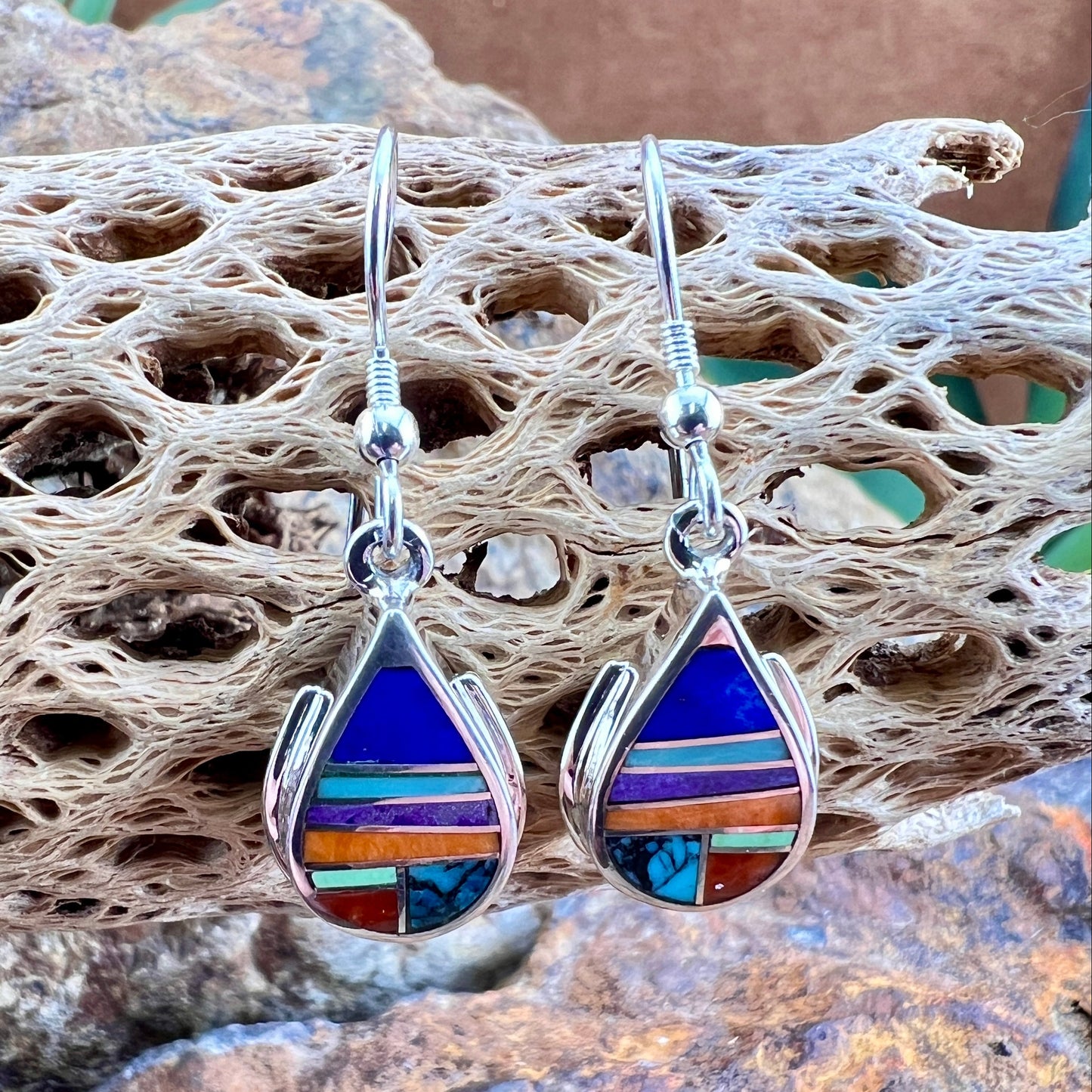 Multicolored teardrop earrings on a textured surface with a natural stone background