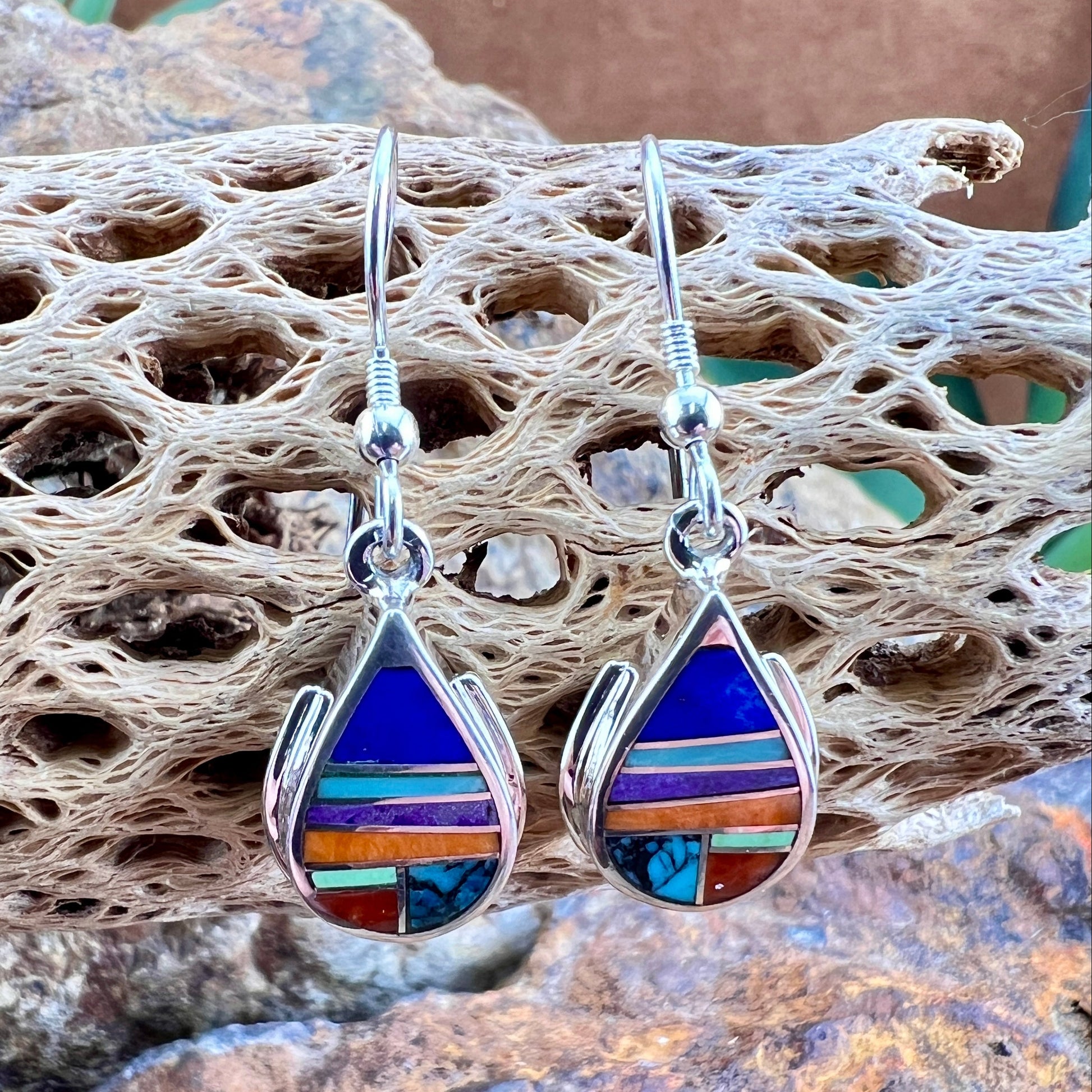 Multicolored teardrop earrings on a textured surface with a natural stone background