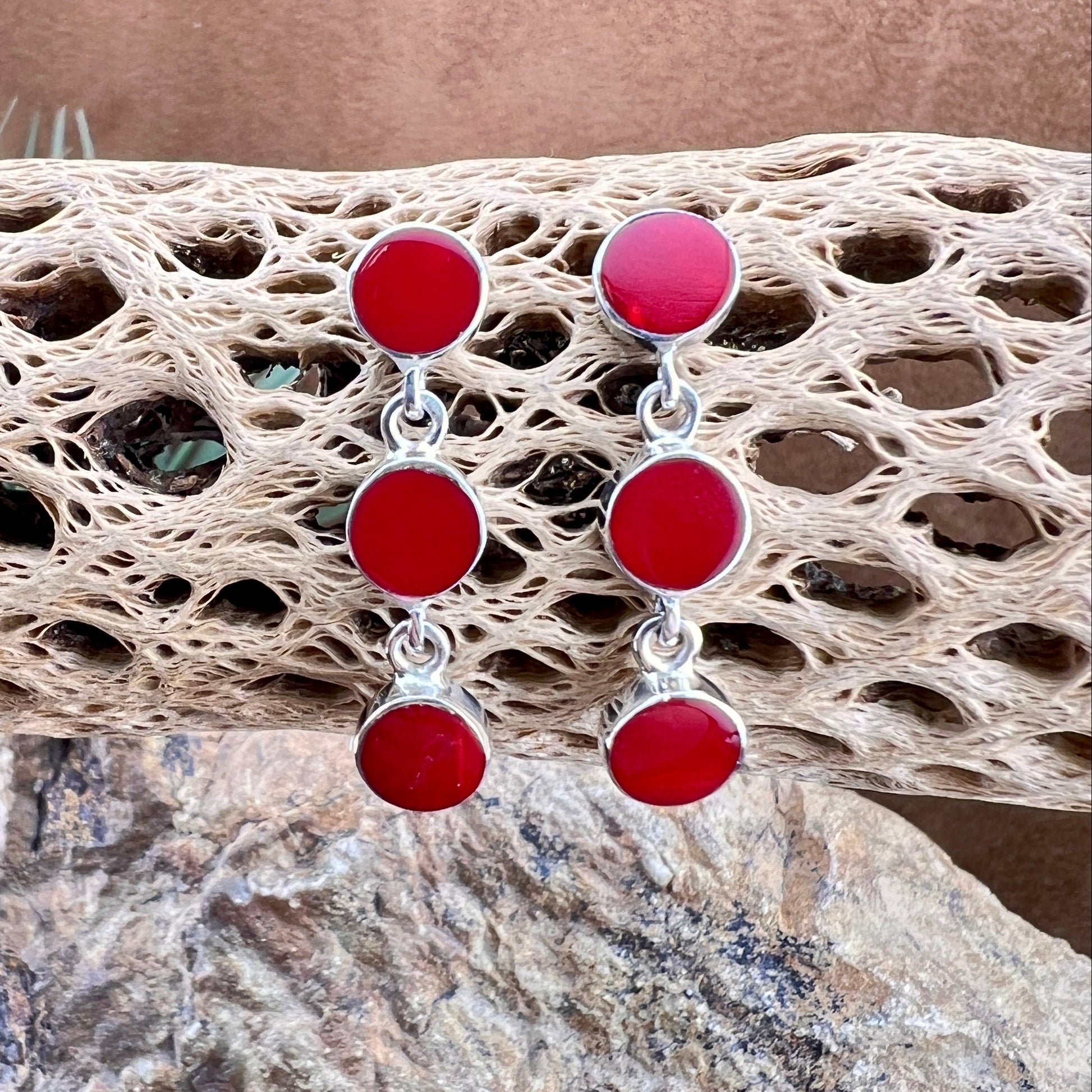 Red and silver earrings on a textured stone surface