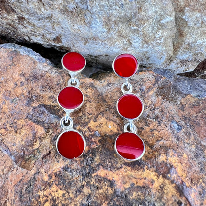 Red circular earrings with silver accents on a stone background