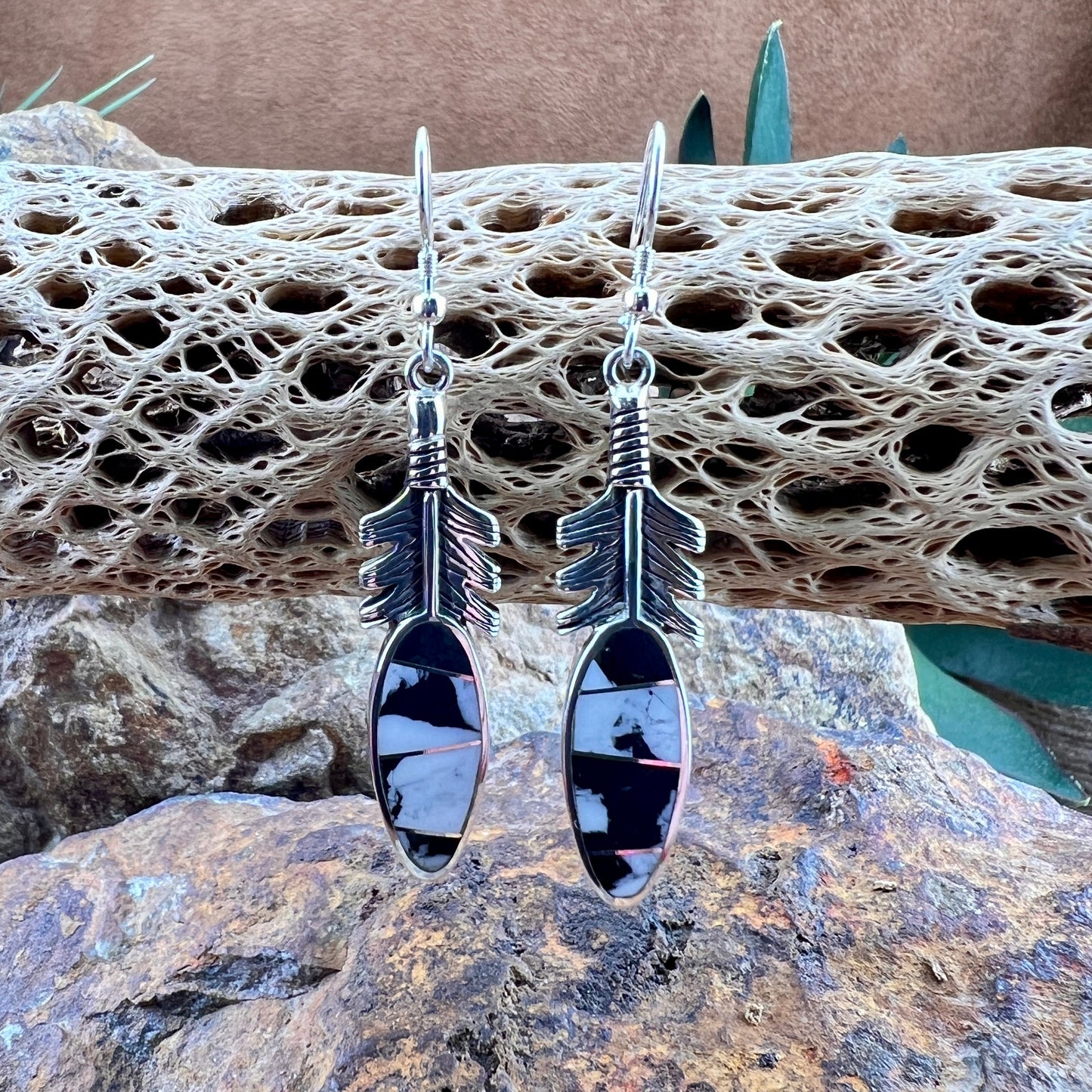 Silver arrow-shaped earrings on a textured stone surface