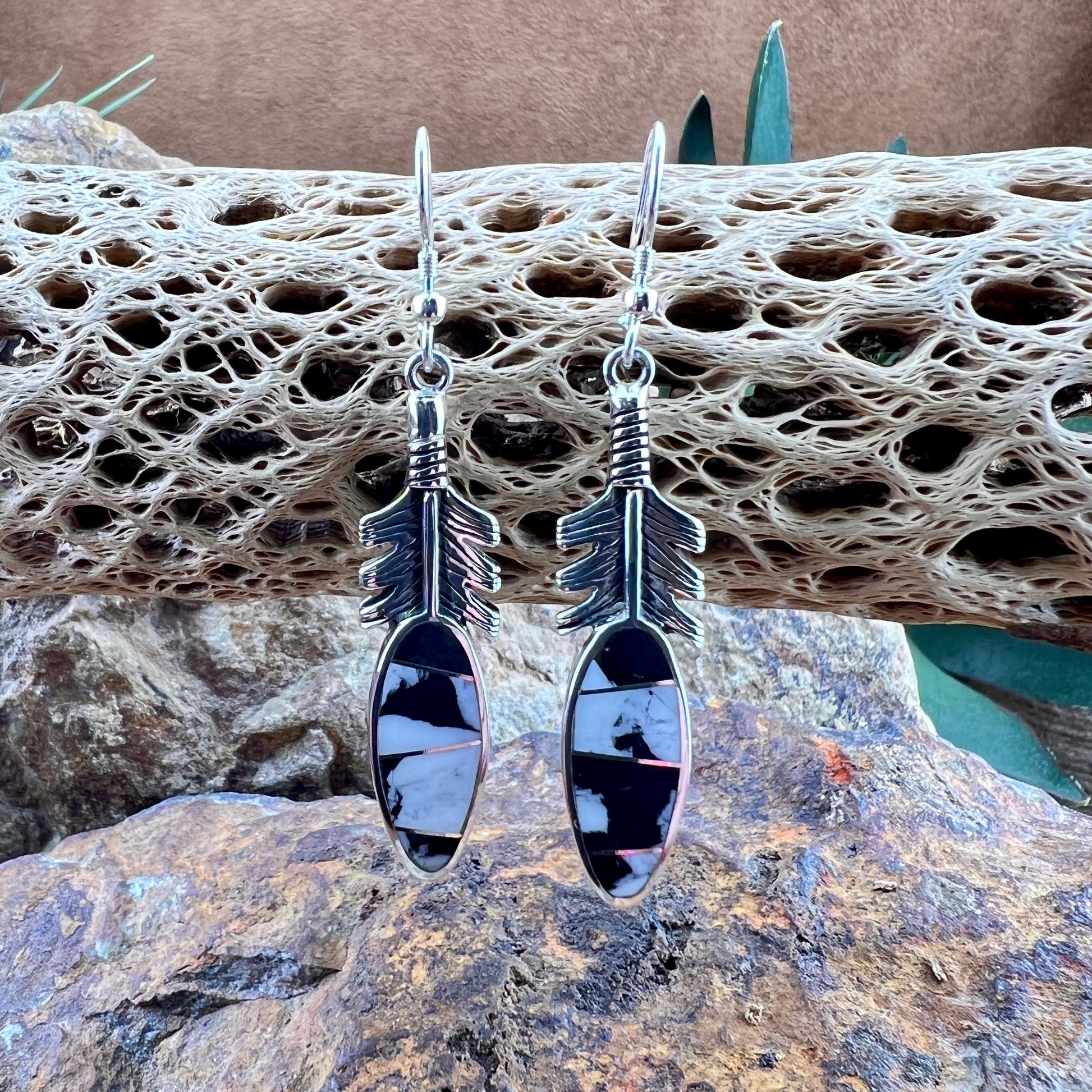 Silver arrow-shaped earrings on a textured stone surface