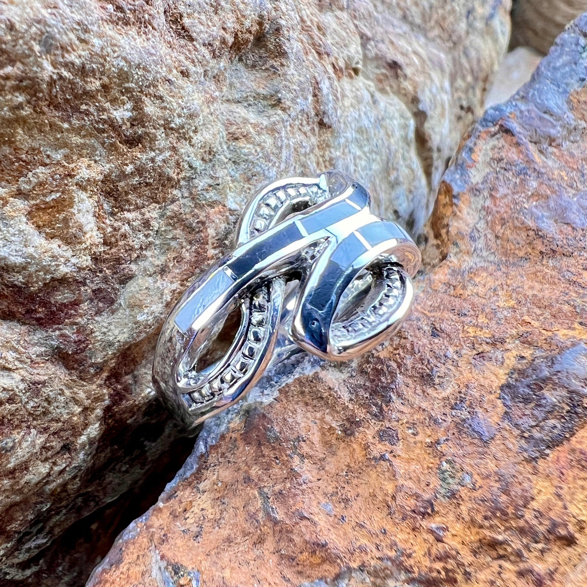 Silver ring with intricate design on a textured stone surface