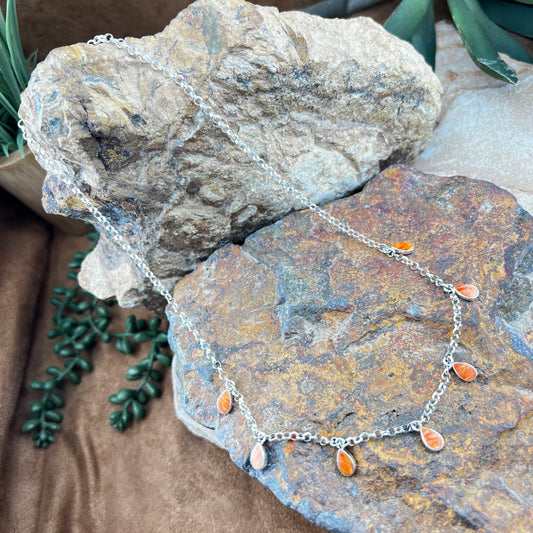 Necklace with orange teardrop pendants on a rock with greenery