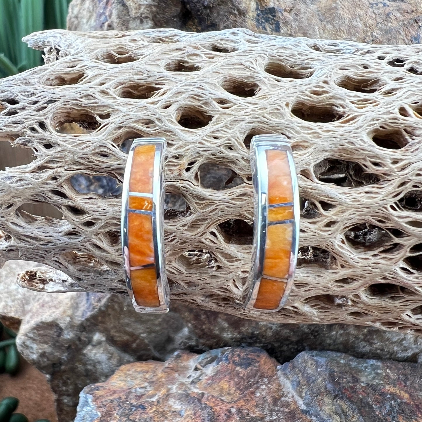 Silver earrings with orange inlay on a textured stone surface