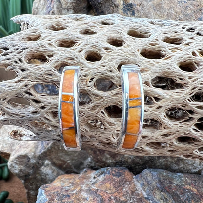 Silver earrings with orange inlay on a textured stone surface