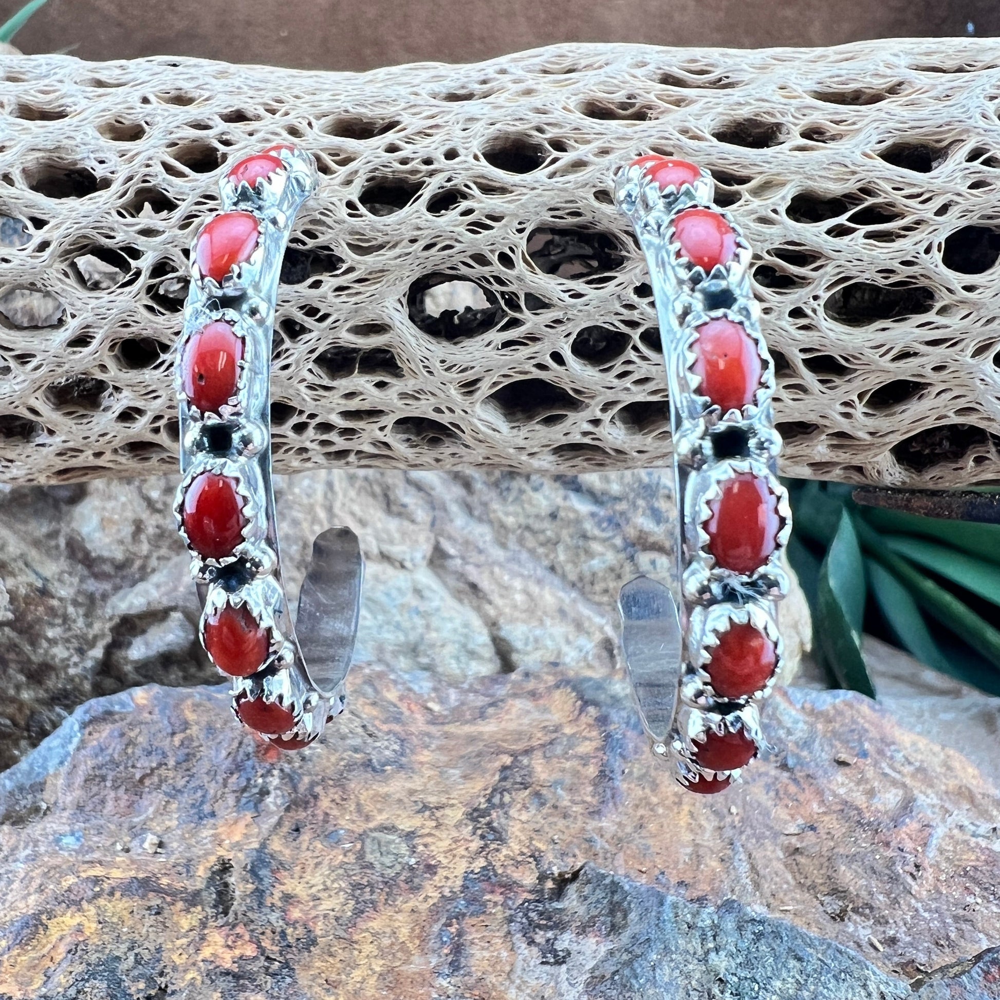 Pair of silver hoop earrings with red stones on a textured stone surface