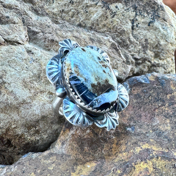 A sterling silver ring with a high-domed oval cabochon of white stone with visible caramel host matrix, set on a rock.