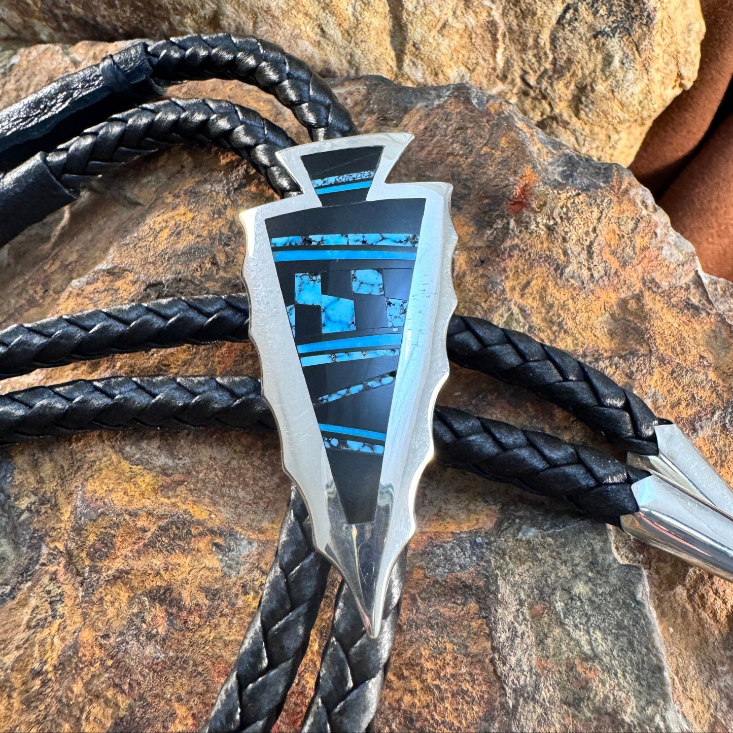 Two metallic arrowheads with black braided strings on a stone surface