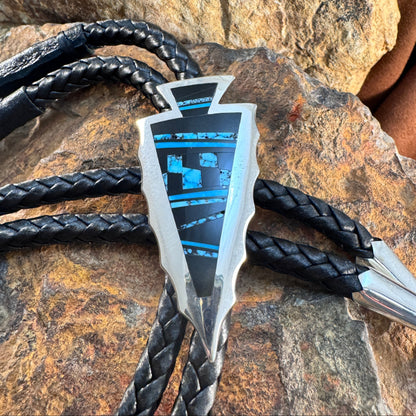 Two metallic arrowheads with black braided strings on a stone surface