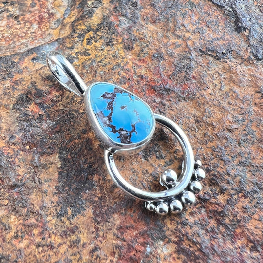 Silver pendant with blue stone on a textured brown surface