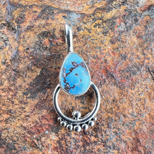 Blue teardrop pendant with silver setting on a textured stone background