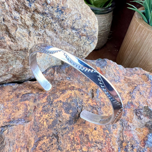 Silver bracelet on a textured stone surface with plants in the background