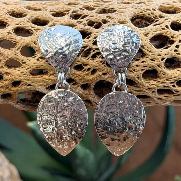 Hammer finished drop earrings by artie yellowhorse. They hang from a piece of driftwood