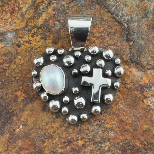 Silver pendant with cross and pearl on a stone background