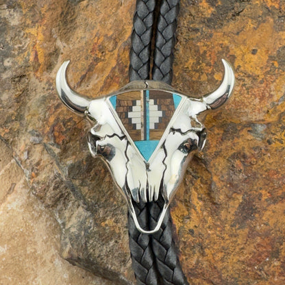 Silver bull skull bolo tie with braided black cord on a stone background