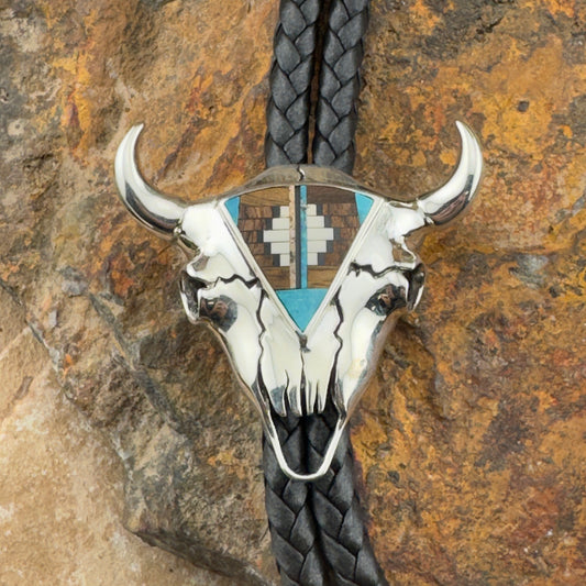 Silver bull skull bolo tie with braided black cord on a stone background