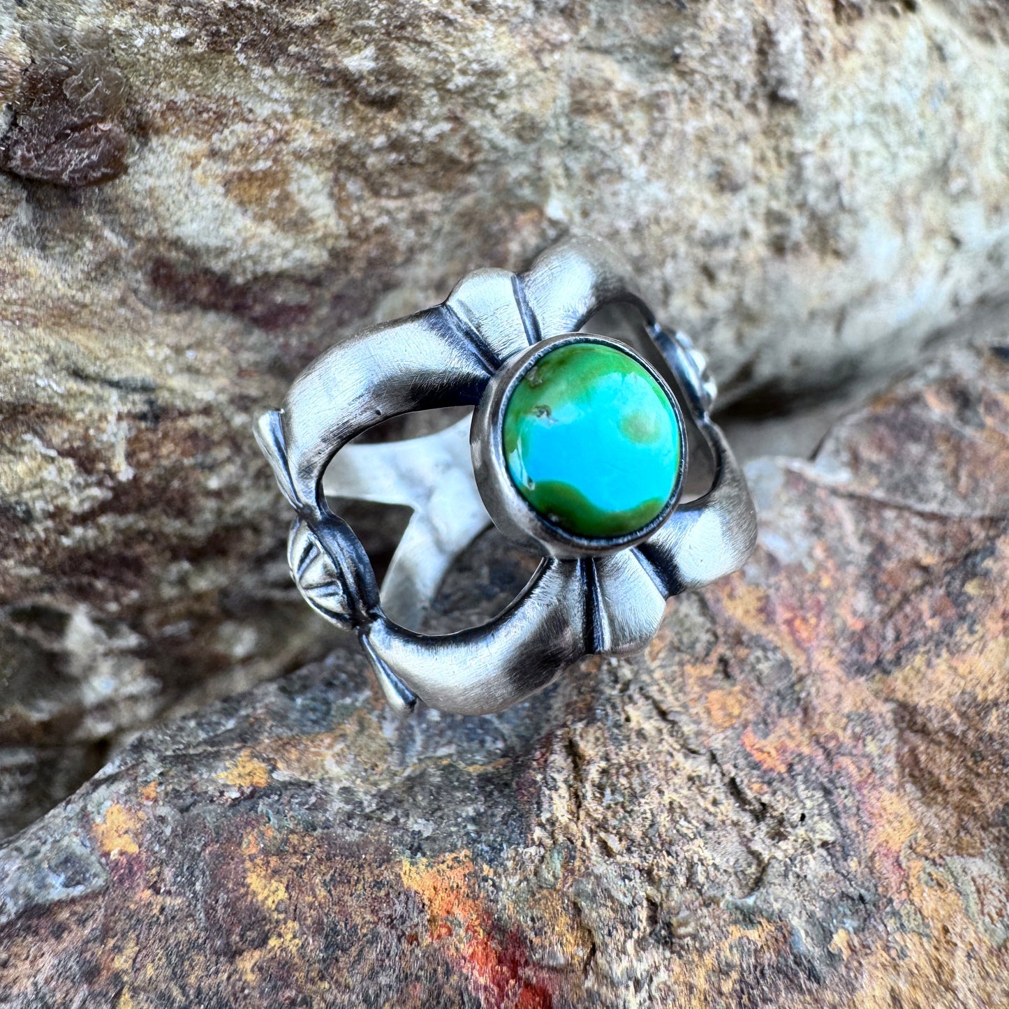 Silver ring with a green stone on a rocky surface