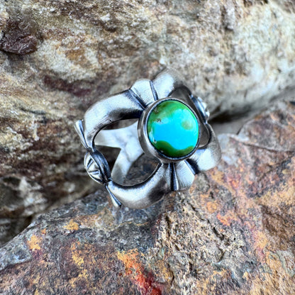 Silver ring with a green stone on a rocky surface