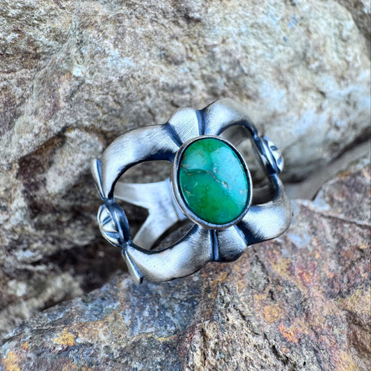 Silver ring with a green stone on a rocky surface