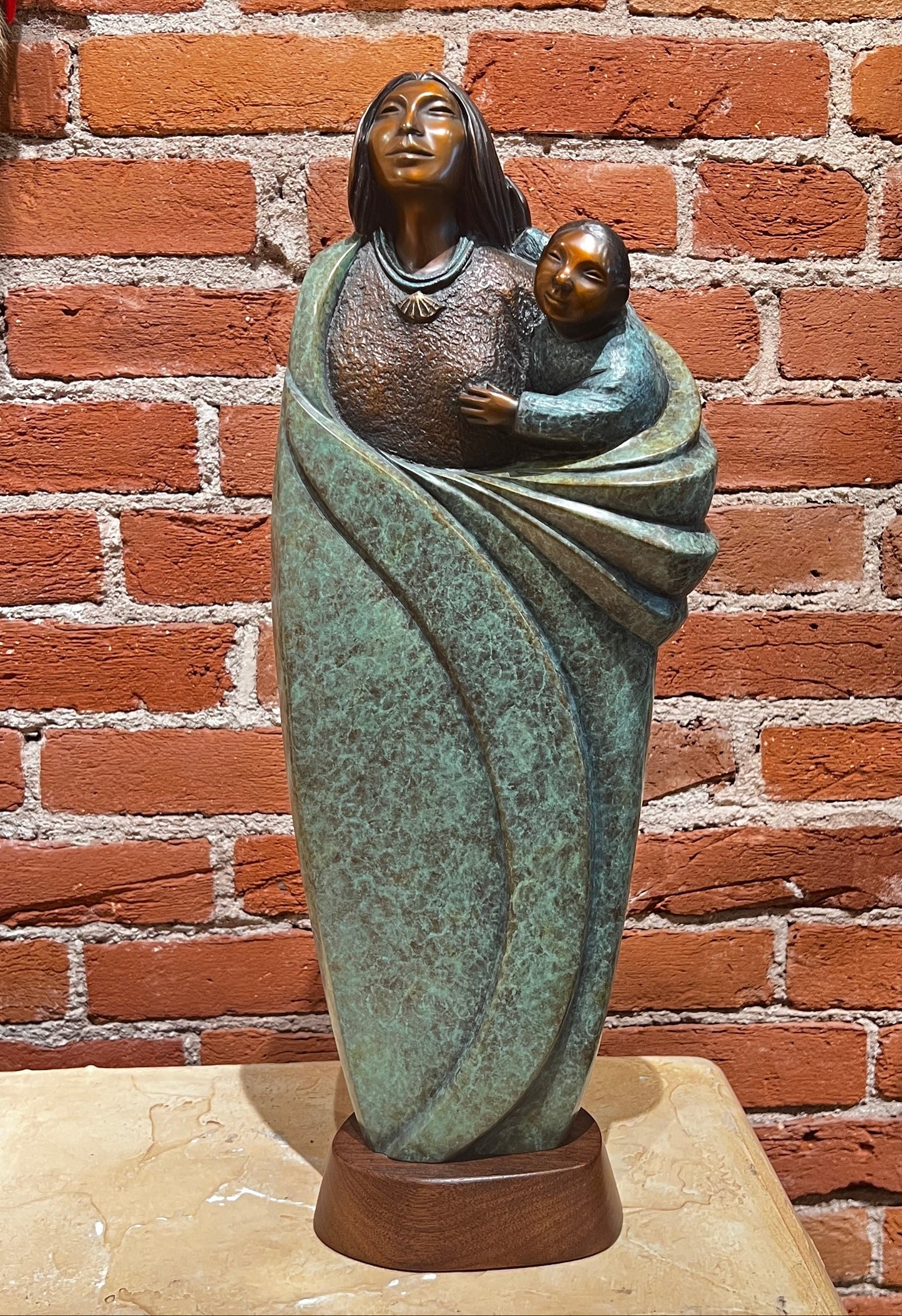 Statue of a mother holding a child against a brick wall.
