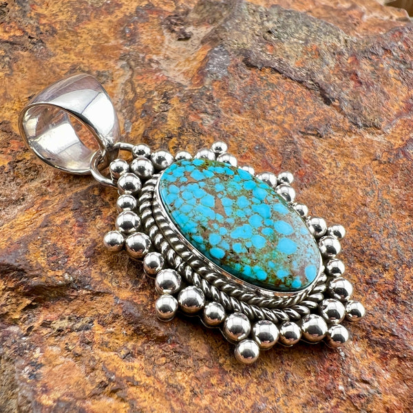 Silver pendant with turquoise stone on a rocky background
