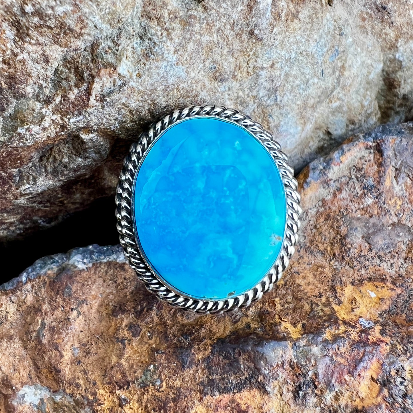 Turquoise stone ring with silver band on a rocky background
