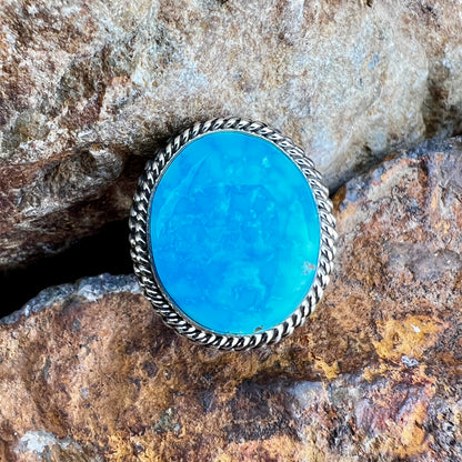 Turquoise stone ring with silver band on a rocky background