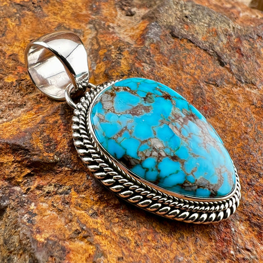 Turquoise pendant with silver setting on a stone background