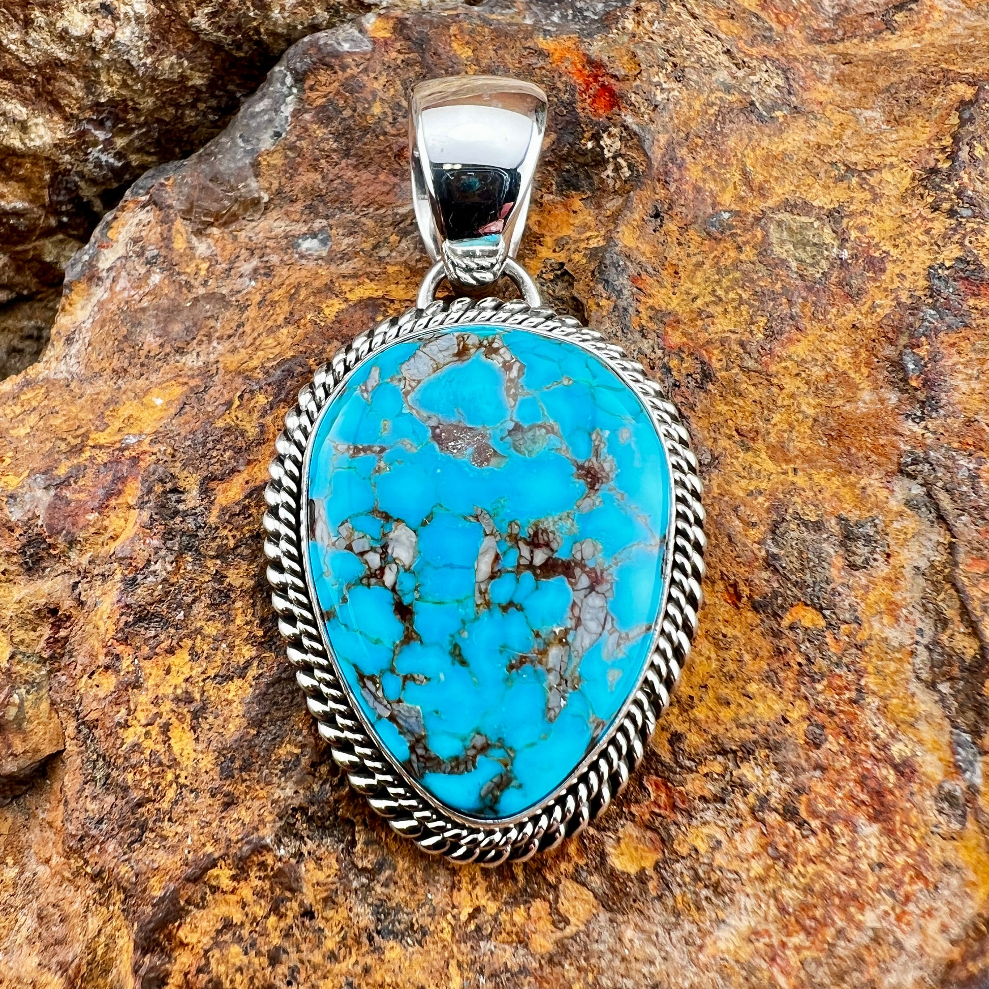 Turquoise stone pendant with silver frame on a rocky background