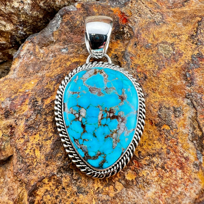 Turquoise stone pendant with silver frame on a rocky background