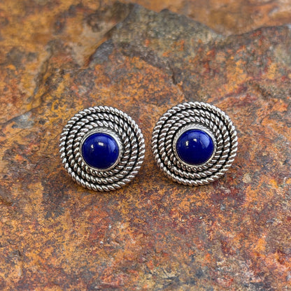 Post earrings with a rope detailing and dark blue center stone, displayed on a rock surface.   