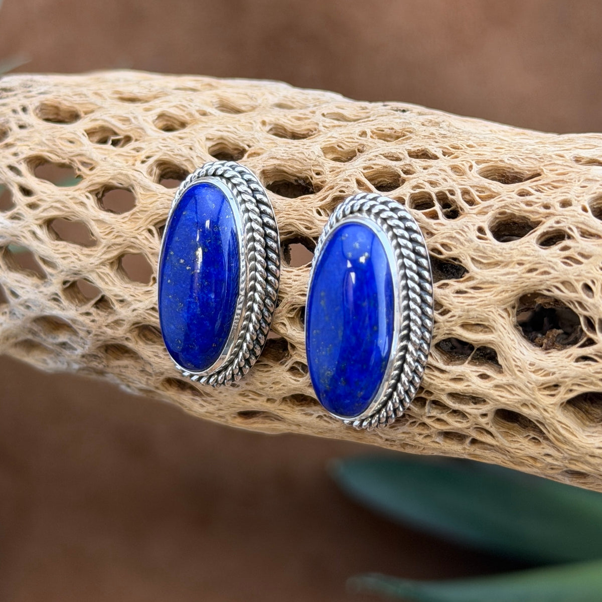 Angled view of sterling silver oval lapis lazuli post earrings with twisted-rope edges