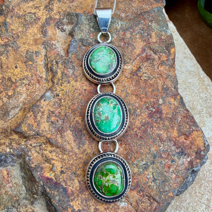 Silver pendant with three green stones on a textured stone surface