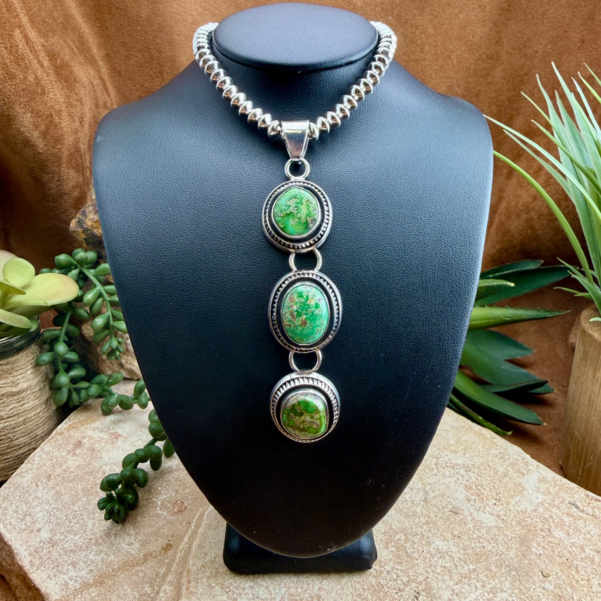 Necklace with three green stones on a black mannequin bust against a natural background