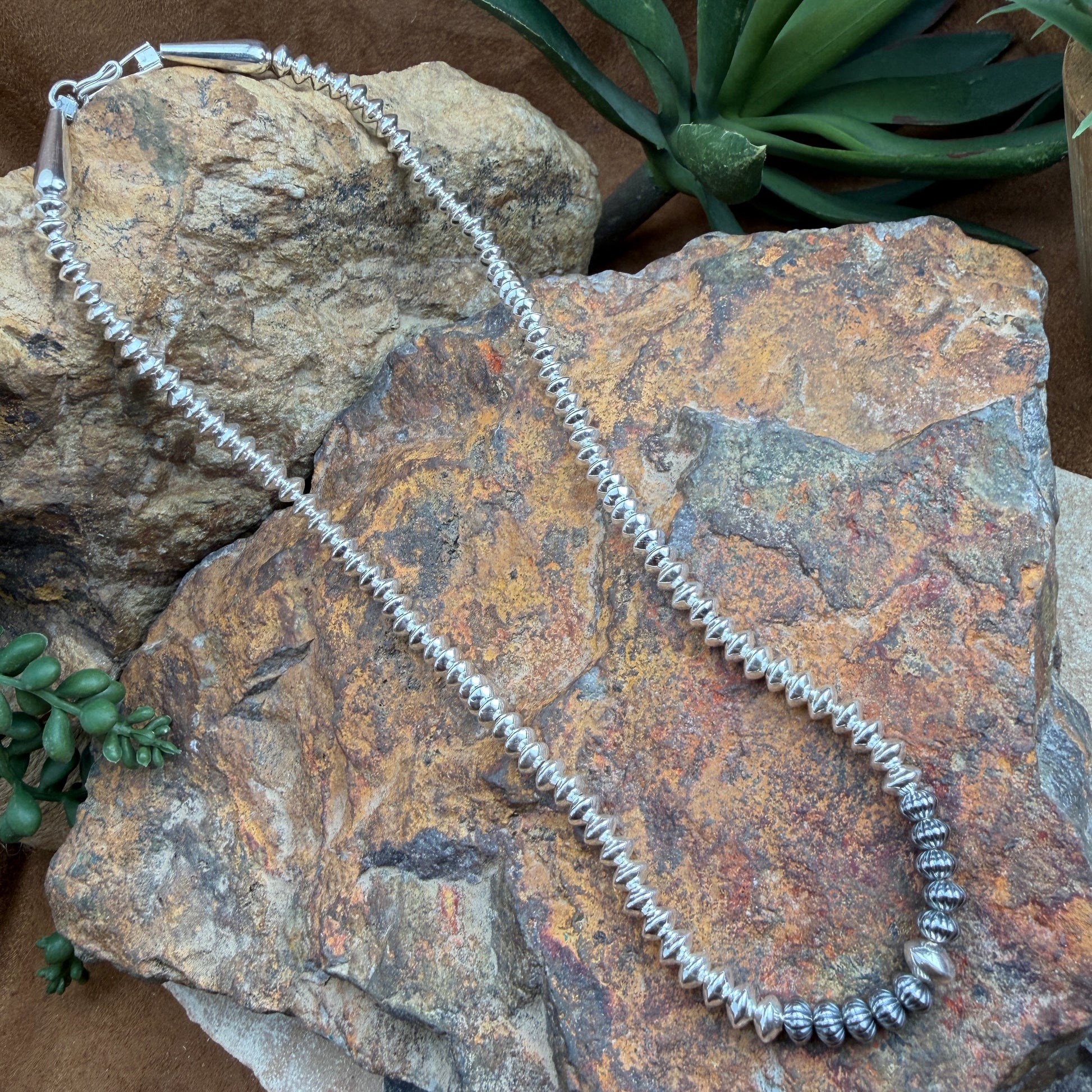 Silver beaded necklace on a textured stone surface with succulents