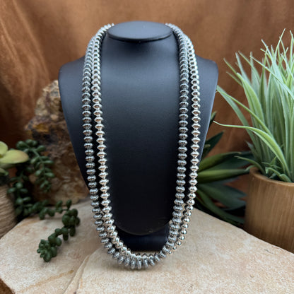 Silver beaded necklace on a black mannequin bust with plants in the background