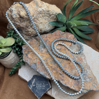 Silver necklace on a textured stone surface with plants