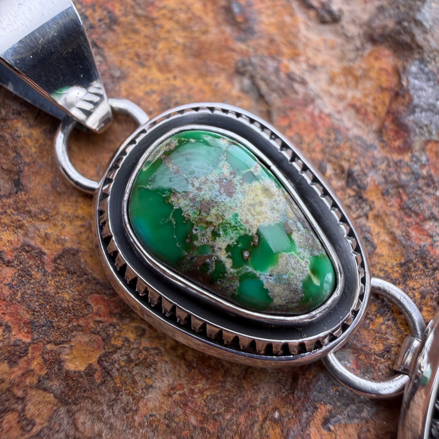 Silver pendant with a green stone on a textured brown background