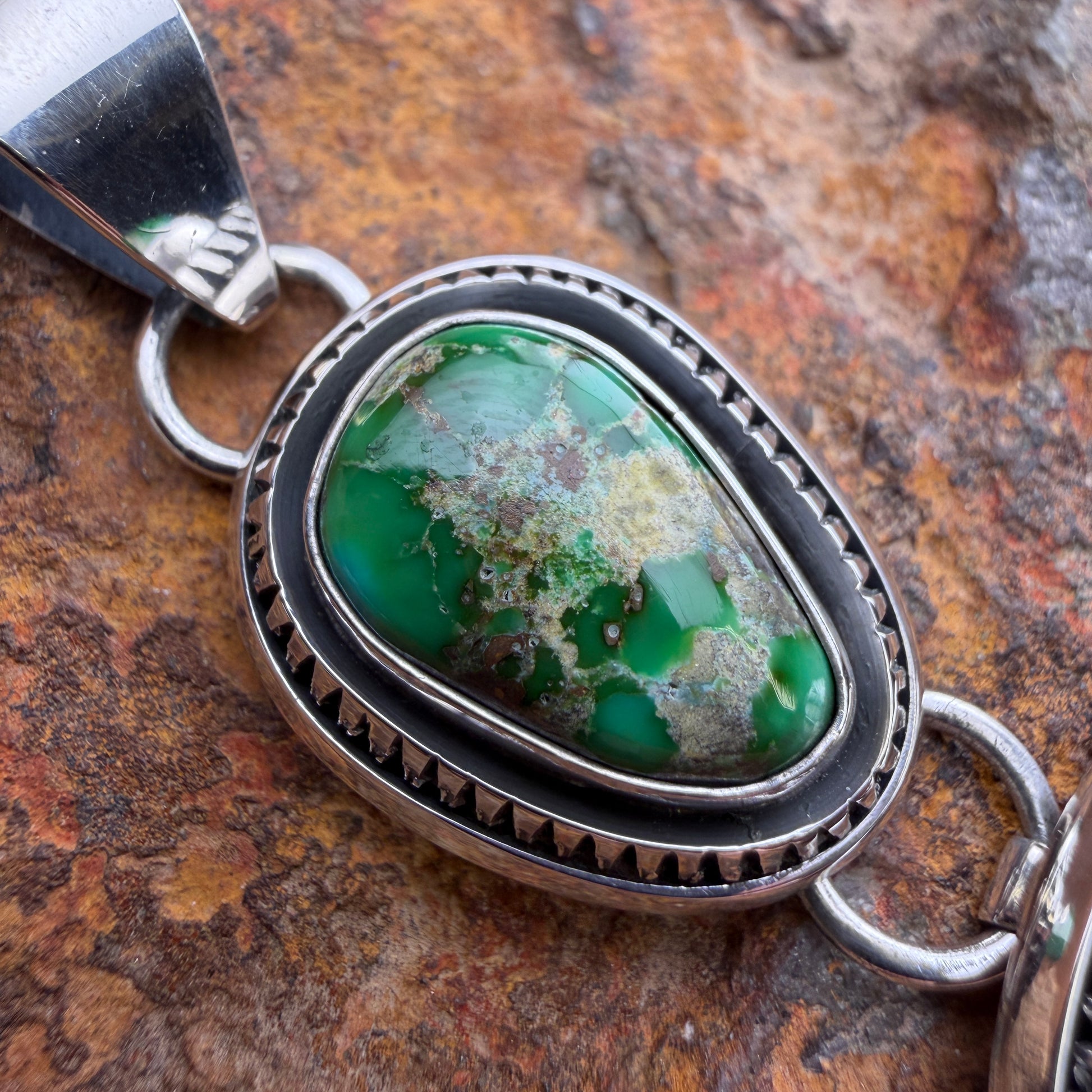 Silver pendant with a green stone on a textured brown background