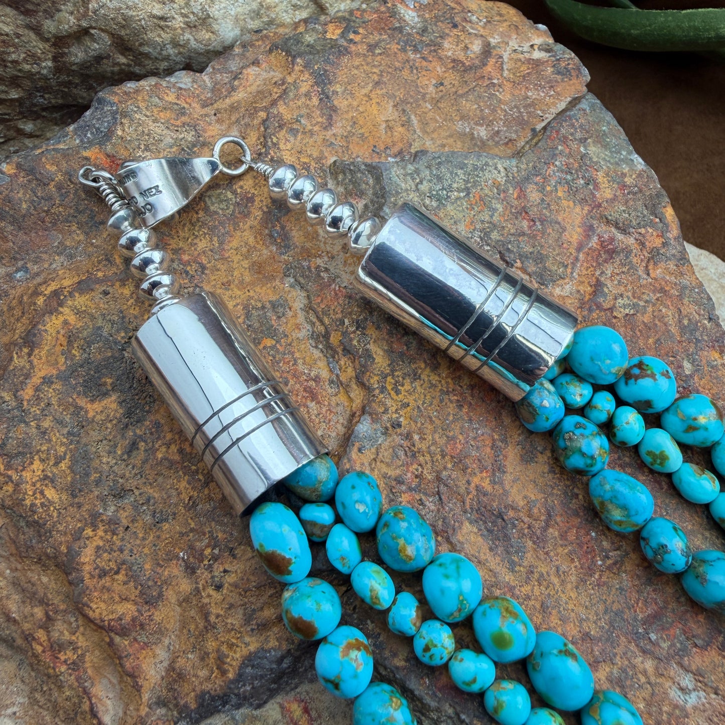 Turquoise beaded necklace with silver clasp and barrels on a textured stone surface