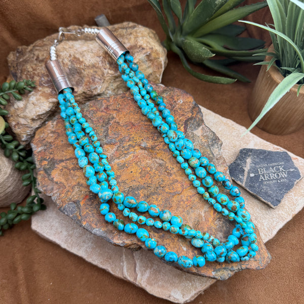 Turquoise beaded necklace on a stone surface with plants in the background