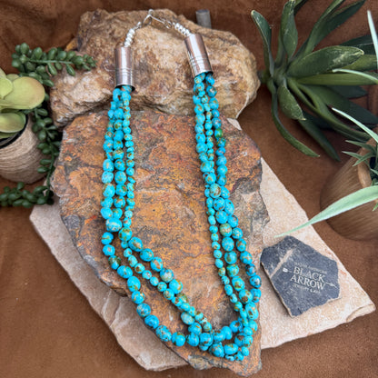 Turquoise beaded necklace on a stone surface with a 'Black Arrow' tag
