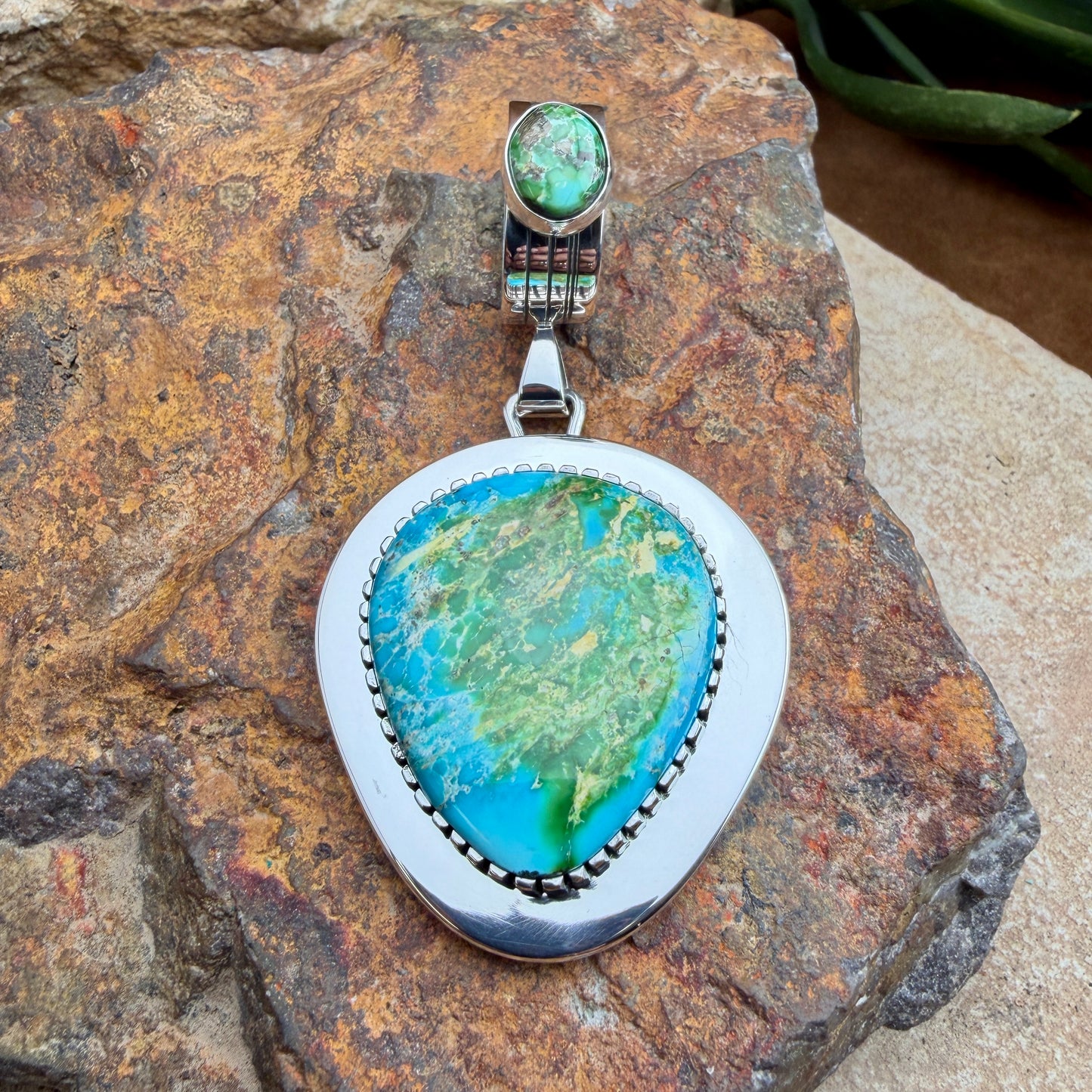 Turquoise stone pendant with secondary bale stone on a rocky surface