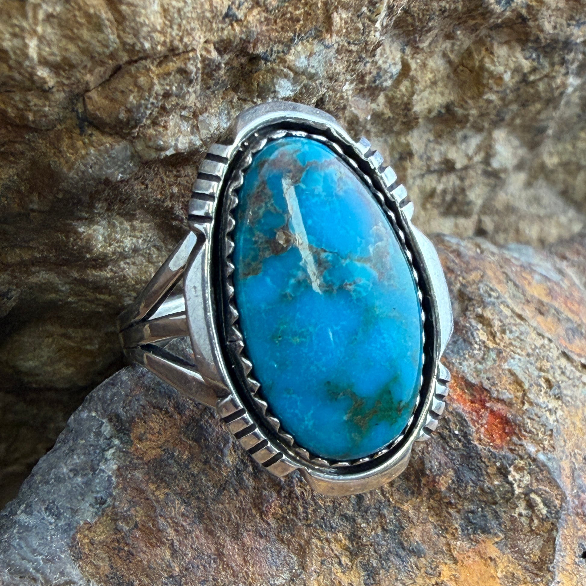 Lone Mountain Turquoise Ring by Ray Coriz - angled front view on rock showing vivid blue oval cabochon with golden matrix and serrated rim